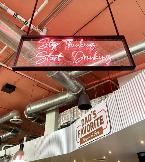 one of the neon signs "stop thinking, start drinking" in the delray beach market food court