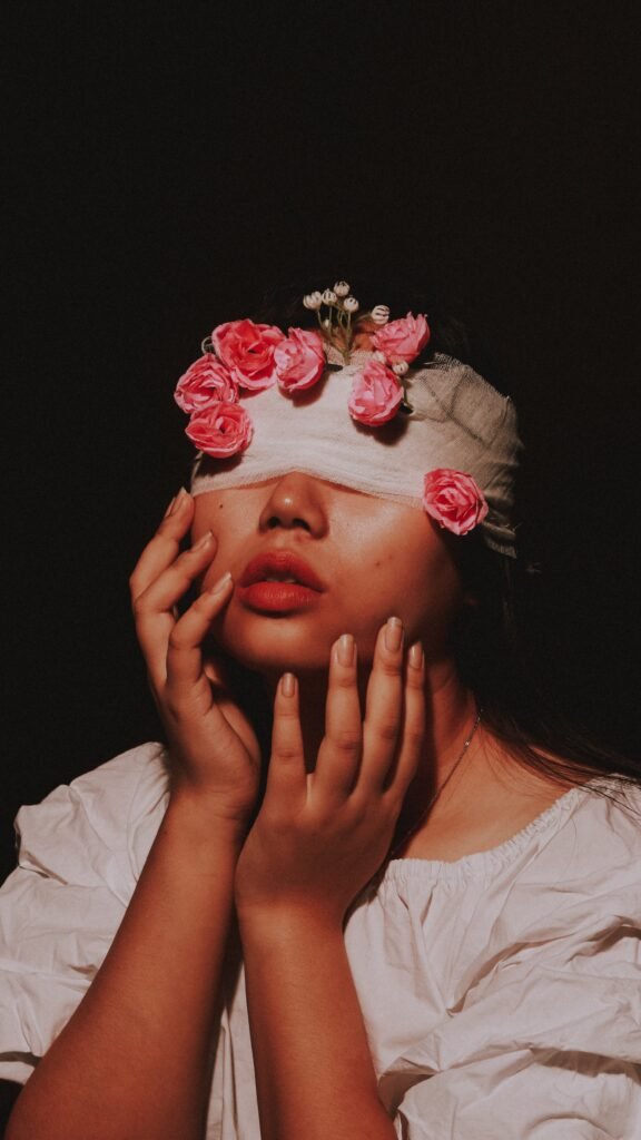 girl blind folded with flowers on the blindfold holding her hand up to her face