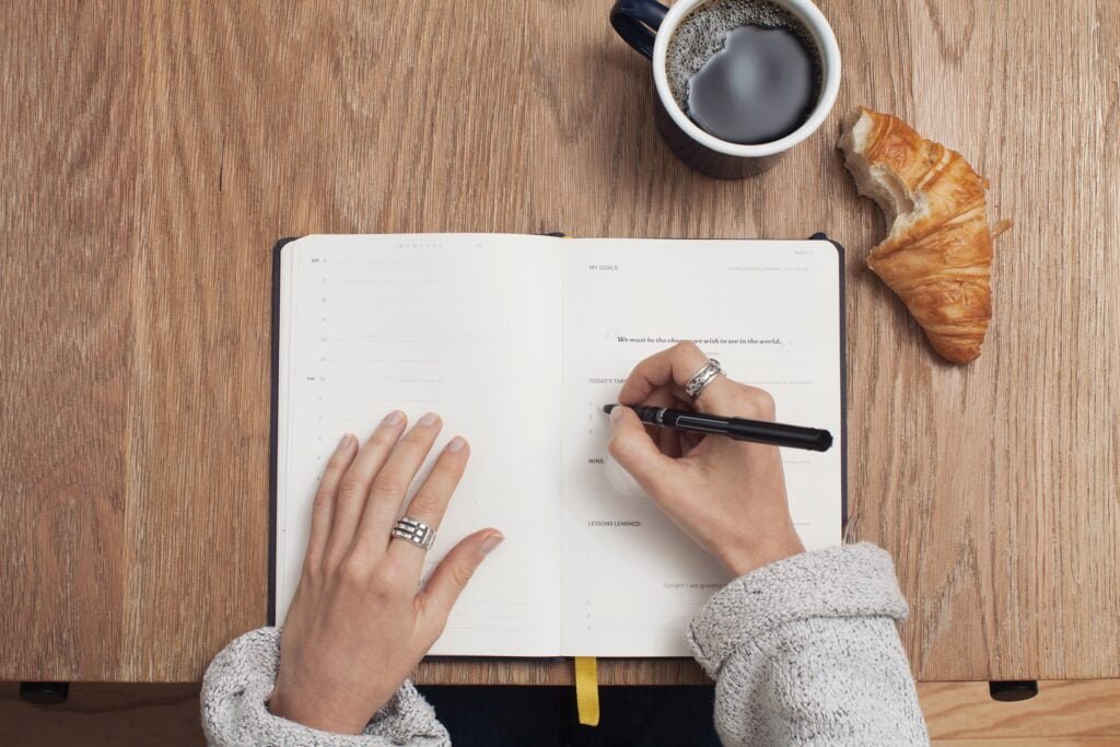 Couple making a bucket list. The pictuer is a womens hands writing in a journal a list of things to do