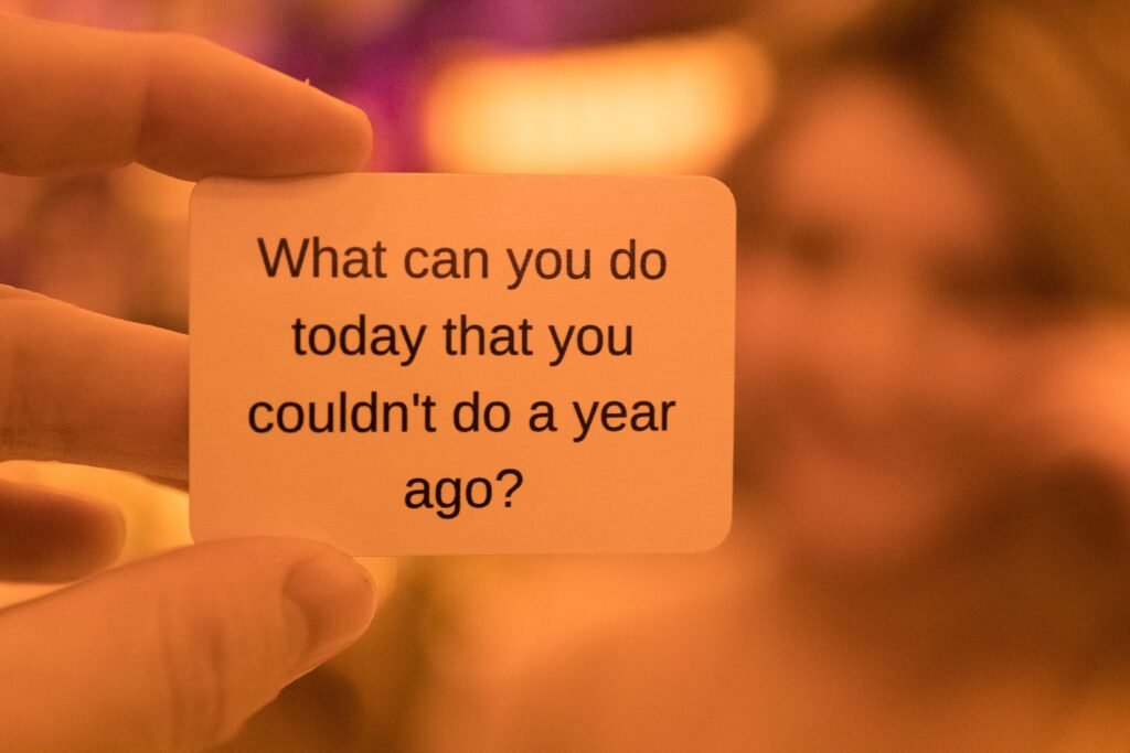 fingers holding a card that says "What can you do today that you couldn't do a year ago?"