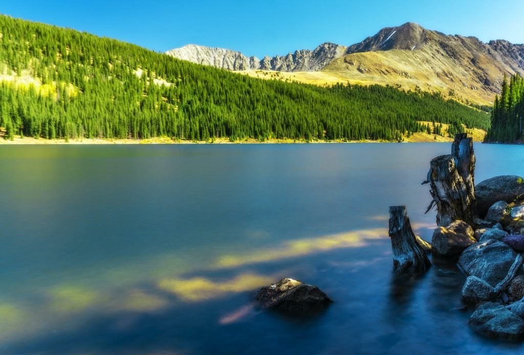 Scenic View Of The Mountains With Green Pine Trees Beside Calm Body of Water - Romantic Things To Do In Colorado