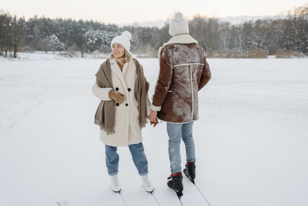 Woman in Brown Coat and Blue Denim Jeans Standing on Snow Covered Ground