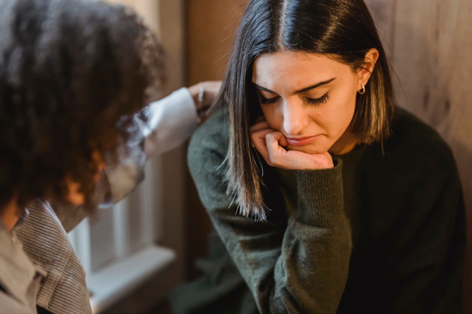 Crop woman tapping shoulder and comforting upset female friend while sitting at home together