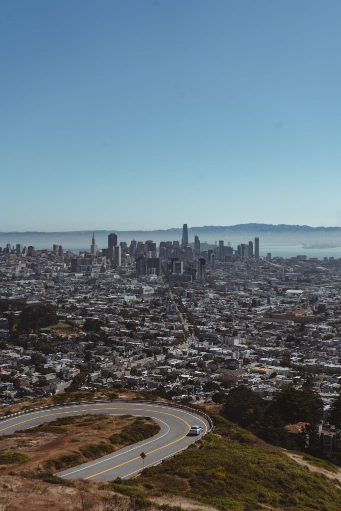 Picturesque scenery of curvy asphalt road going through hilly terrain above San Francisco City with modern skyscrapers against cloudless blue sky