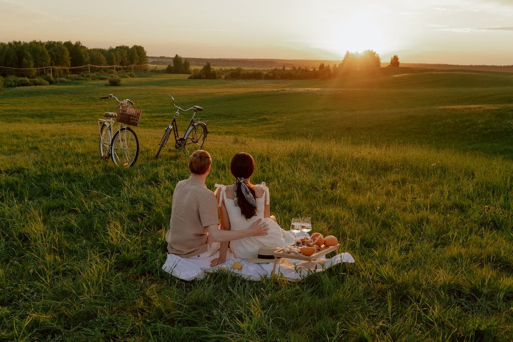 Back View of a Couple Sitting Near Their Bicycles during a sunset picnic