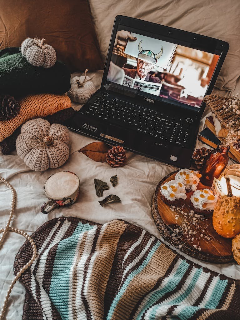 Laptop on Bed with Knitwear and Pastries on Wooden Board