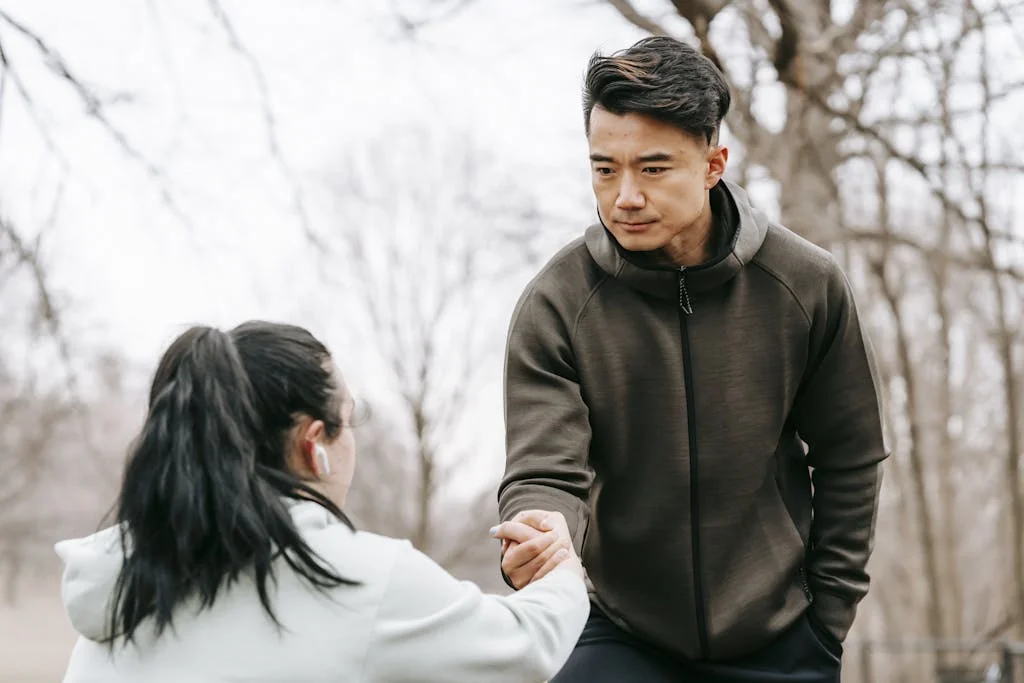 Calm Asian man in sportswear giving hand to unrecognizable female with dark hair in earphones in autumn park in daytime