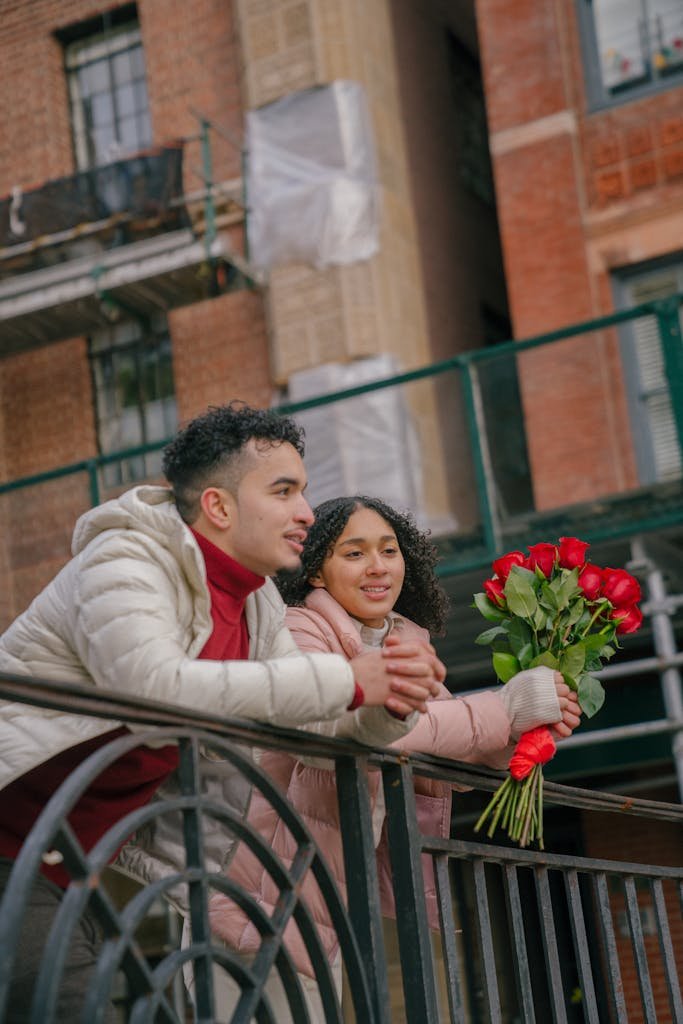 Loving young couple standing on bridge with bouquet of red roses