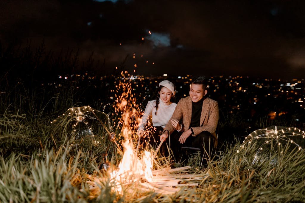 Smiling Asian couple basking near bonfire in evening