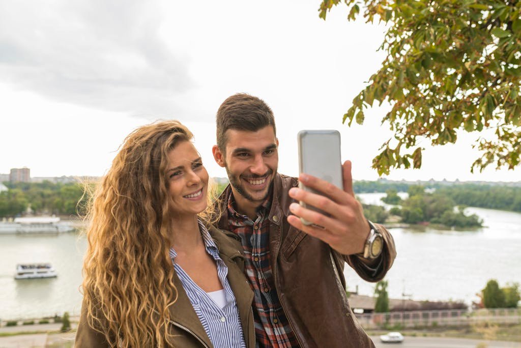 Man Holding Smartphone Beside Woman Near Tree