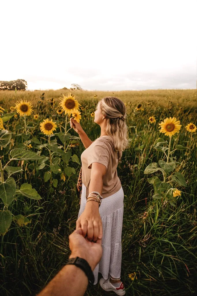 Faceless woman standing on sunflower field and holding boyfriends hand