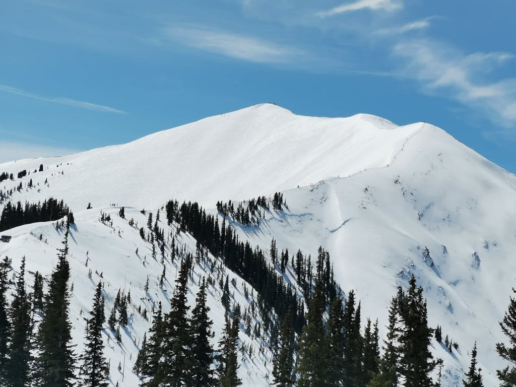 Scenic winter view of snow-covered mountain peaks and evergreen trees in Aspen, Colorado.