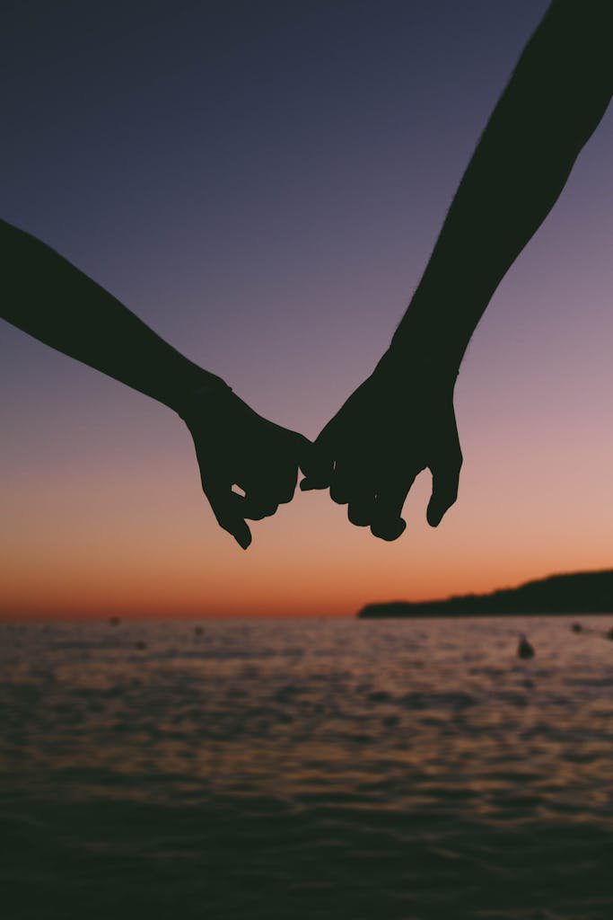 Silhouetted hands holding at sunset over a calm ocean. Romantic and peaceful seascape.