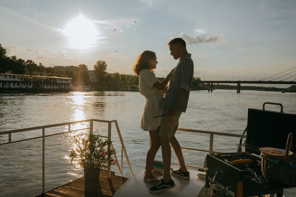 A couple enjoys a romantic moment on a yacht with a stunning sunset over the river, evoking feelings of love and adventure.