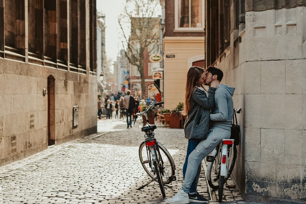 A romantic couple shares a kiss on a bicycle in a charming city alleyway, creating a tender urban moment.