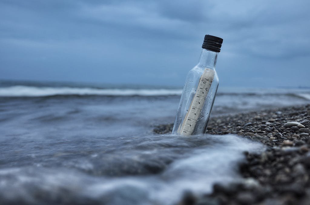 A serene image of a message in a bottle on a rocky beach with waves crashing at dusk.