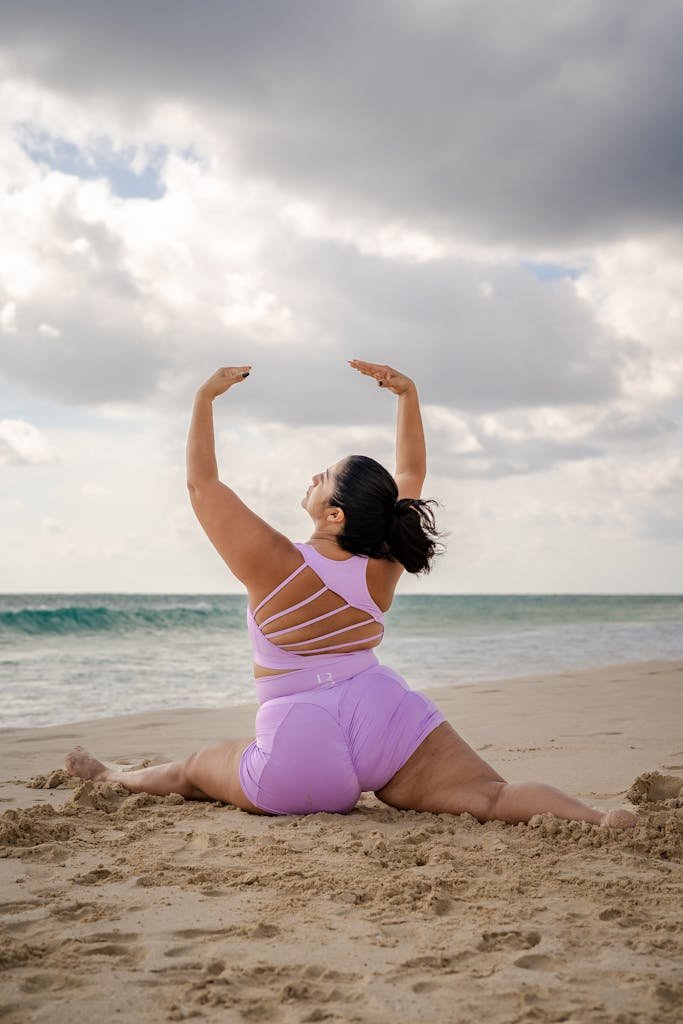 A woman performs yoga on a sandy beach, showcasing strength and flexibility in a serene coastal environment.