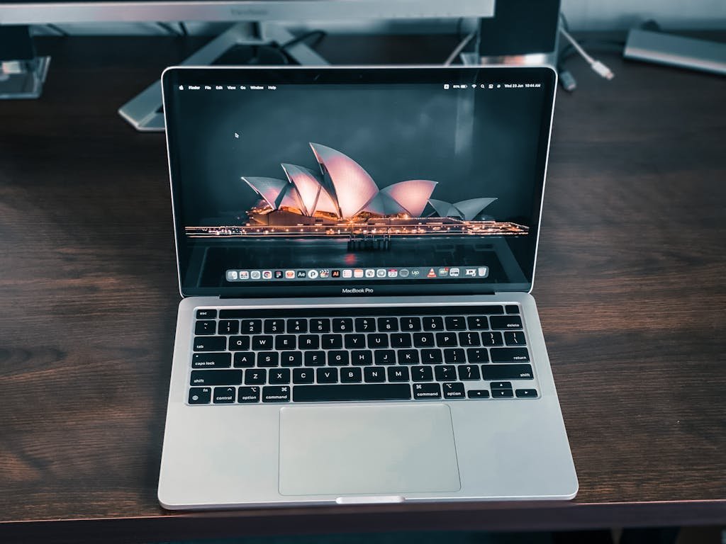 Close-up of a MacBook Pro on a desk with Sydney Opera House wallpaper on the screen.