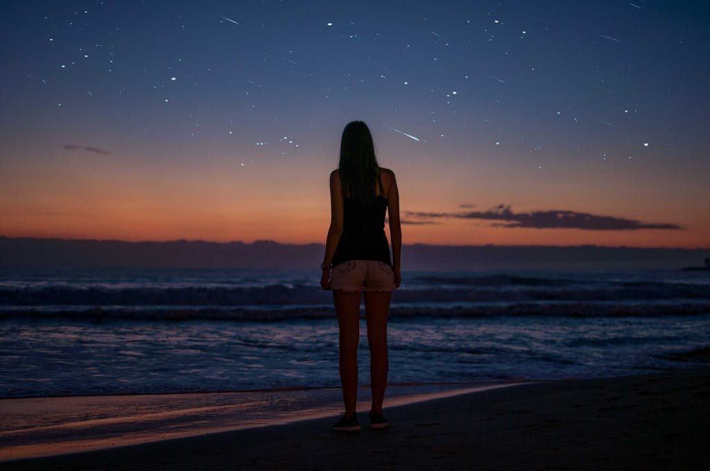 Silhouette of a woman gazing at the starry sky by the beach during twilight. Captivating seascape with waves during a beach date night