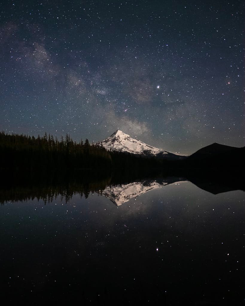 Snow-capped Mount Hood reflected in a serene lake under a starry sky, Oregon.