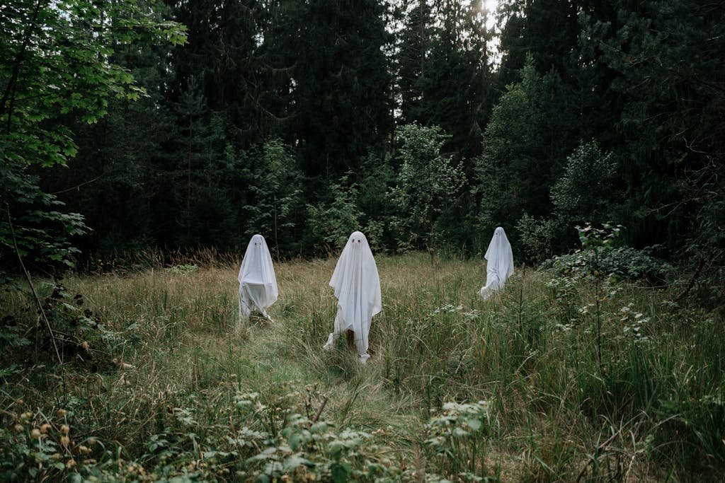 Three people dressed as ghosts in a forest setting evoke Halloween mystery and spirit.