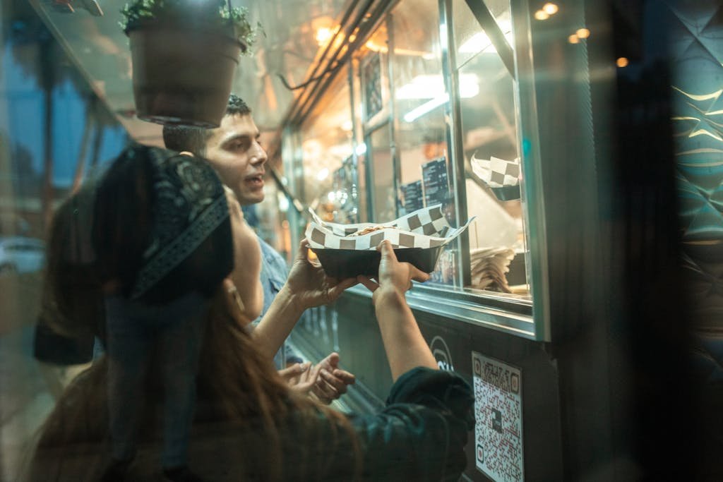 A couple enjoys ordering food from a vibrant street food truck at night.