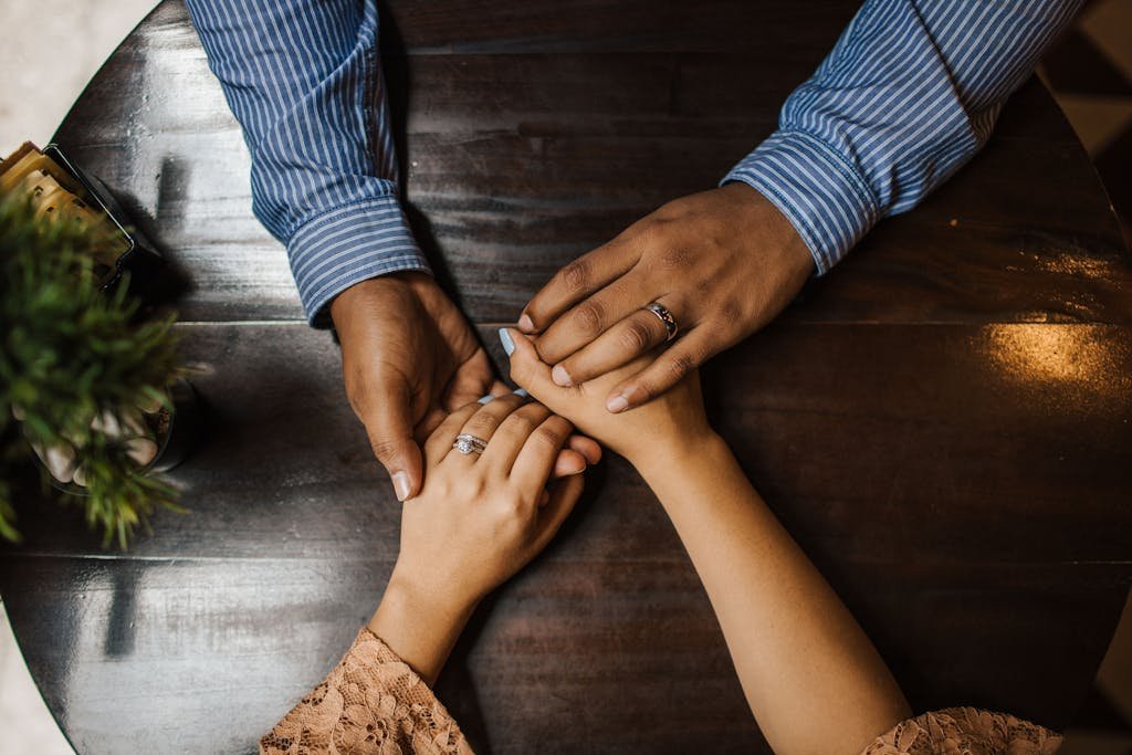 A couple holding hands on a wooden table, expressing love and connection.