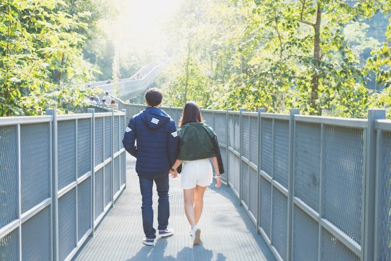 A couple strolling through a lush forest on a sunlit walkway, embracing nature and togetherness.