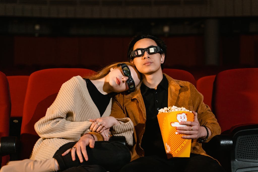 A cozy couple wearing 3D glasses, sharing popcorn in a cinema setting.