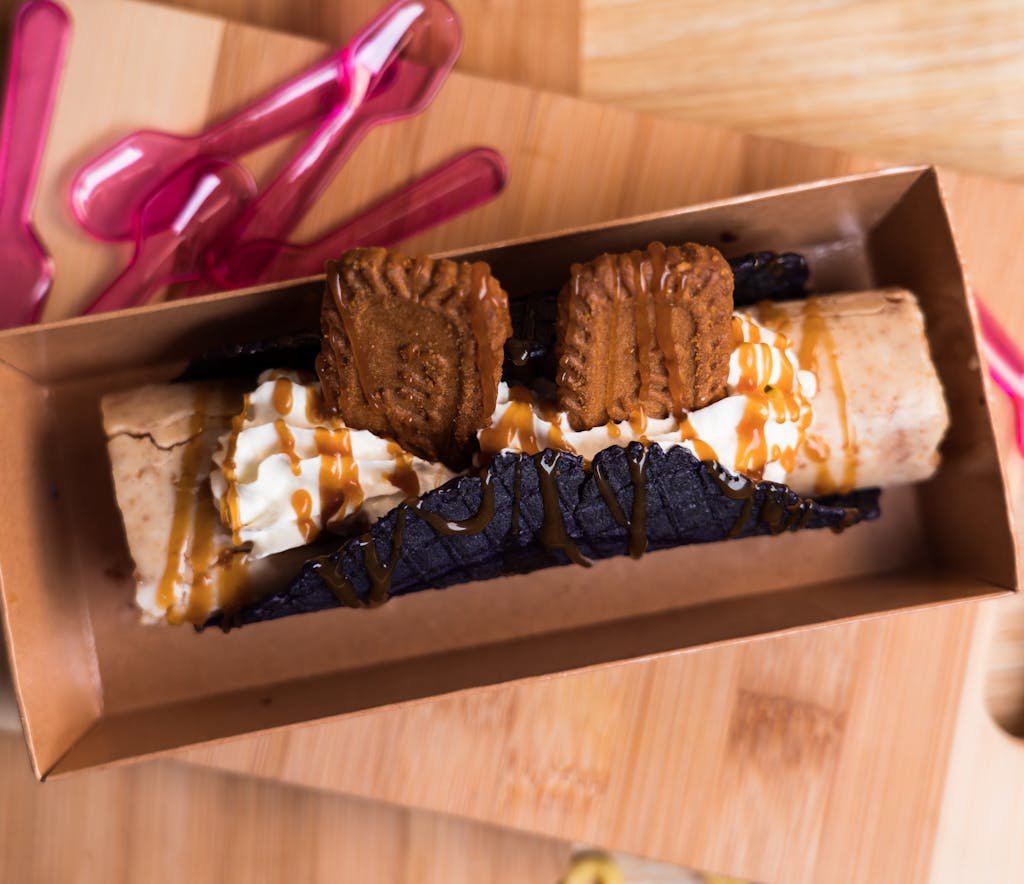 A gourmet dessert taco with cookies, cream, and caramel sauce in a cardboard box.