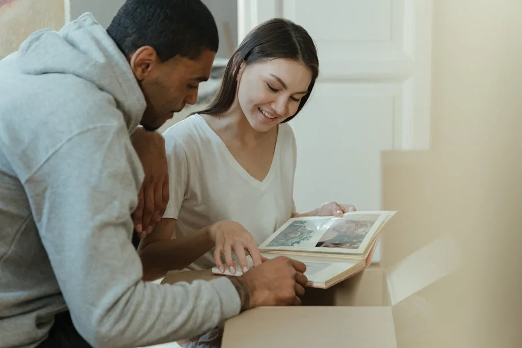 A happy couple reminiscing over photo albums while unpacking in their new home.