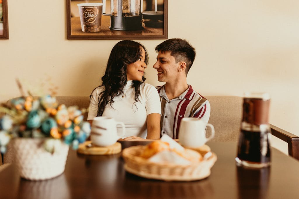 A happy couple smiles at each other in a cozy café setting, enjoying their time together.