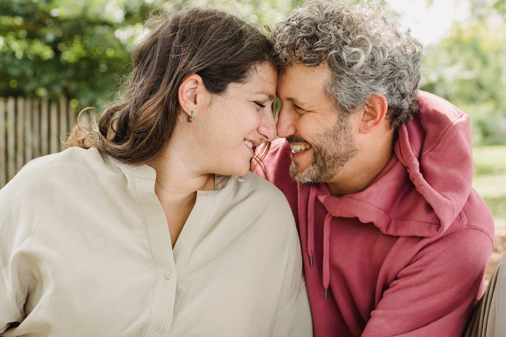 A joyful couple embracing and smiling at each other in a sunny outdoor setting.