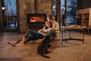 A loving couple relaxes by the fireplace with their dog, enjoying a cozy indoor atmosphere.