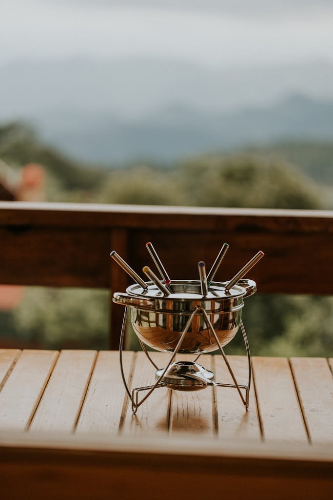 A metal fondue pot with skewers on a wooden table outdoors.