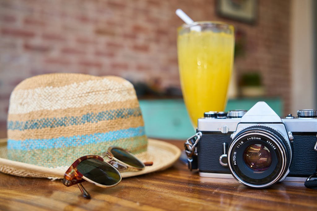 A stylish scene showcasing a vintage camera, hat, and orange juice, evoking summer travel vibes.