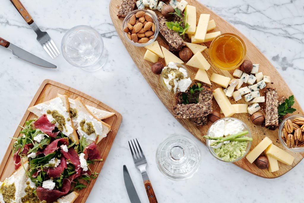 A top view of assorted cheeses, nuts, meats, and bread on a wooden charcuterie board.