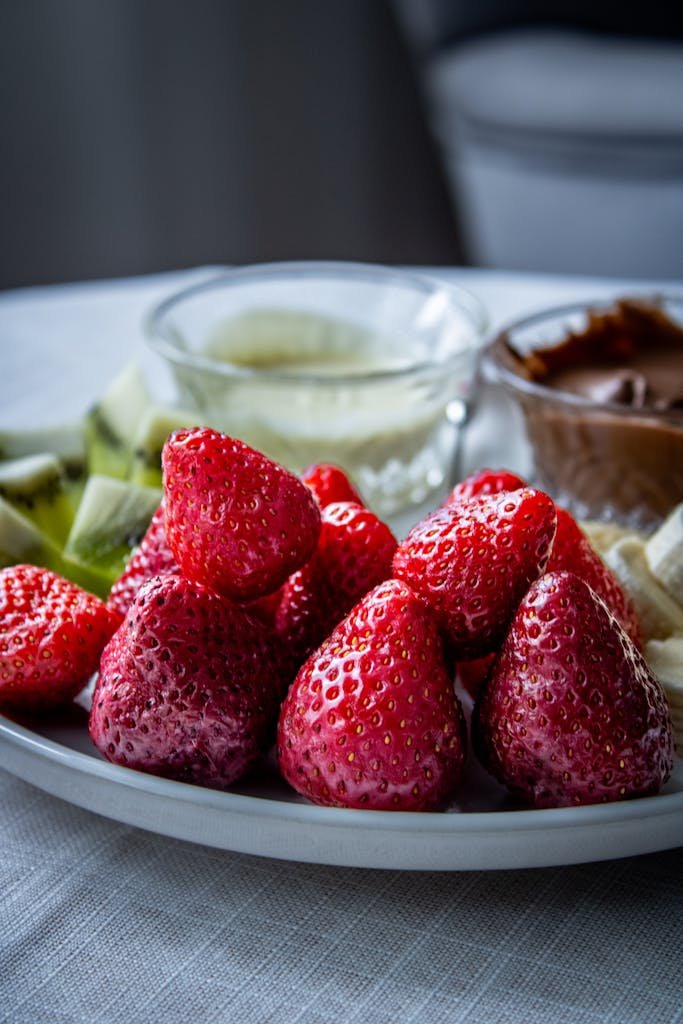 A vibrant plate of fresh strawberries with kiwi slices and chocolate dip ready to enjoy.