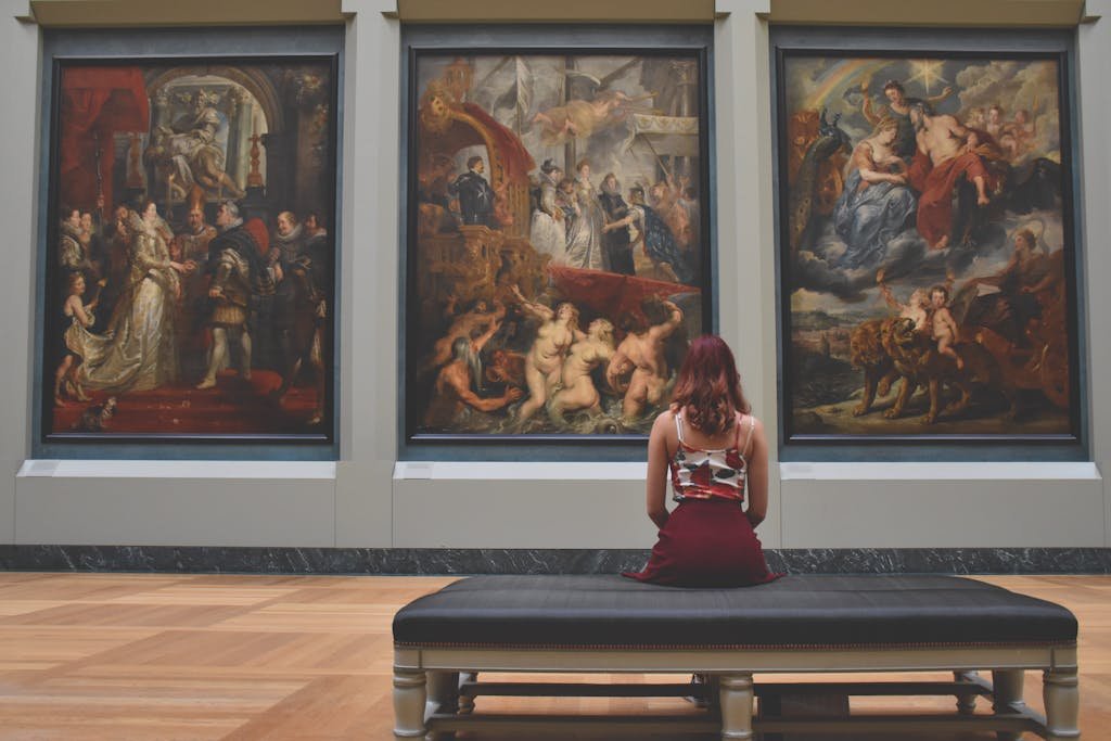 A woman observes classic paintings in an elegant museum gallery.