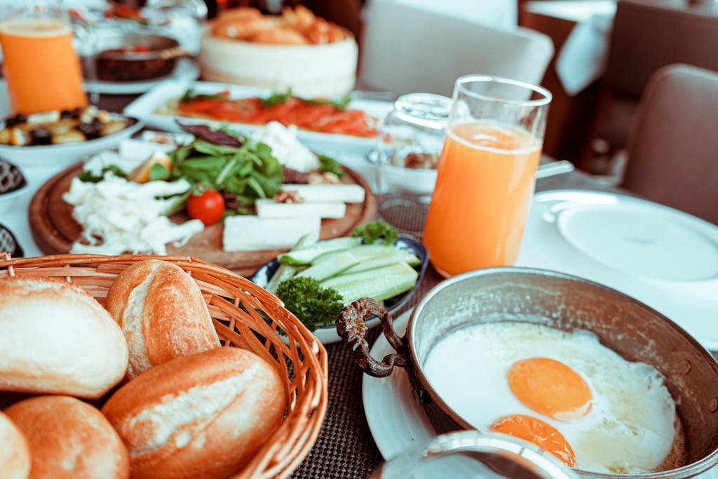 Appetizing breakfast table with orange juice, fried eggs, breads, and fresh vegetables.