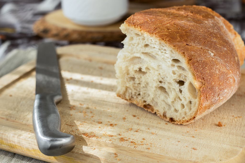 Close-up of a freshly cut loaf of bread on a wooden cutting board with a knife beside it.