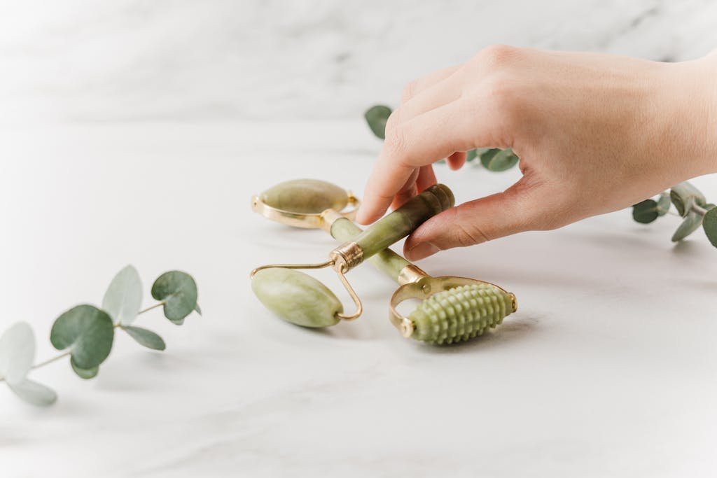 Close-up of a hand holding jade rollers on a marble surface for skincare and wellness.