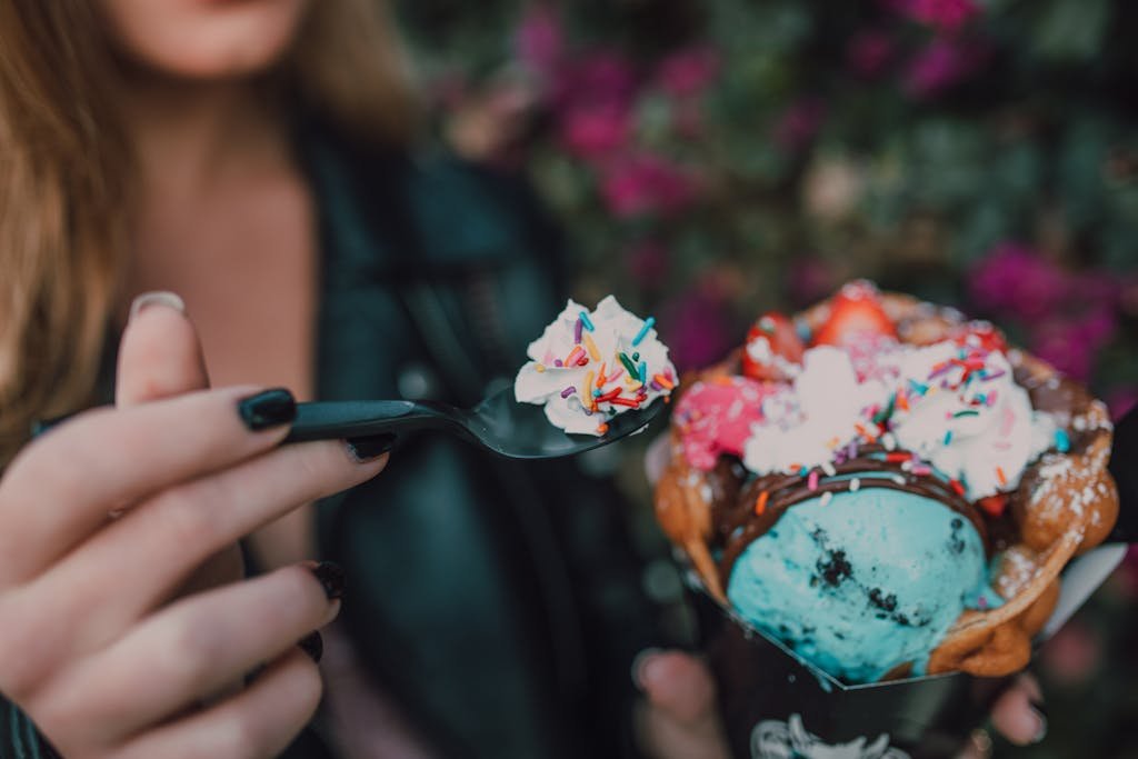 Close-up of a vibrant ice cream dessert with waffle cone and sprinkles, held by a woman.