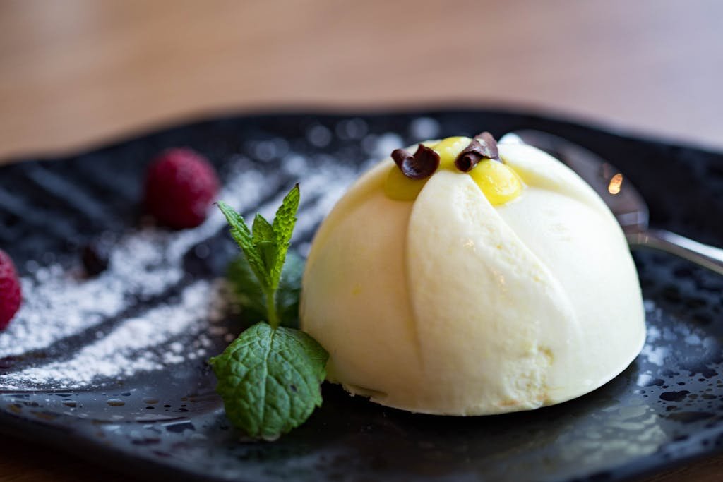 Delicious lemon mousse dessert garnished with fresh raspberries, mint, and chocolate curls on a black plate.