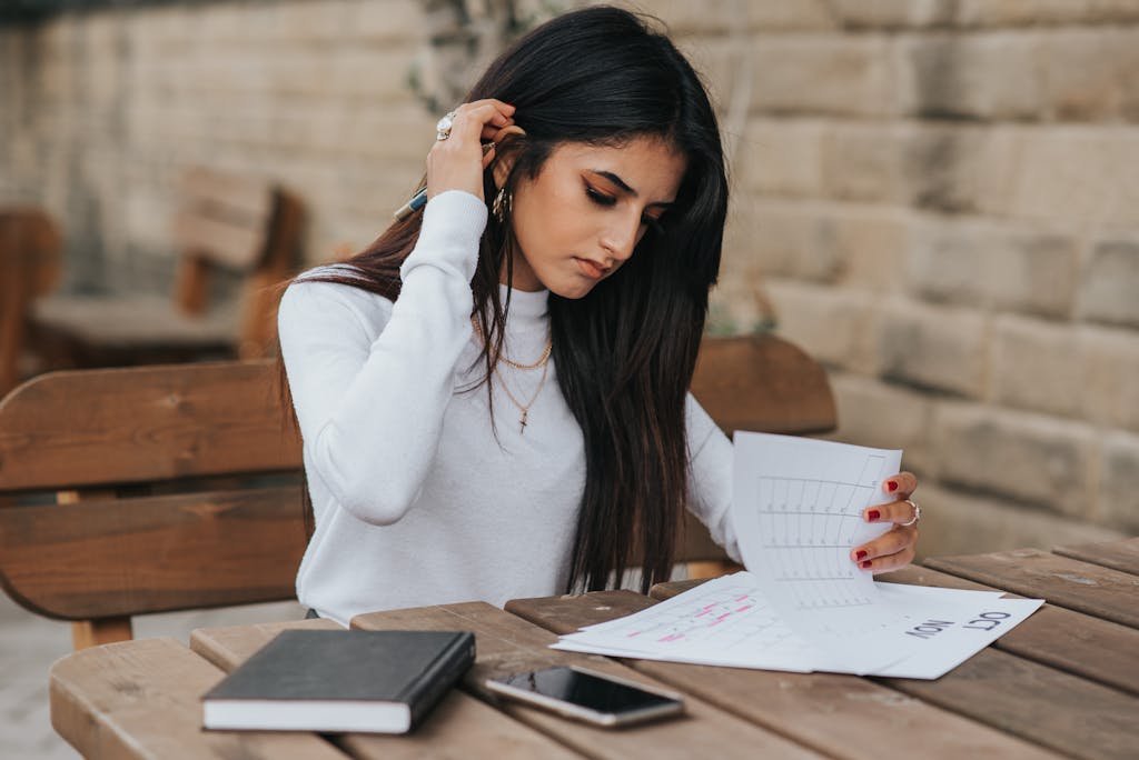 Focused young woman reviewing schedule outdoors with notebook and smartphone.