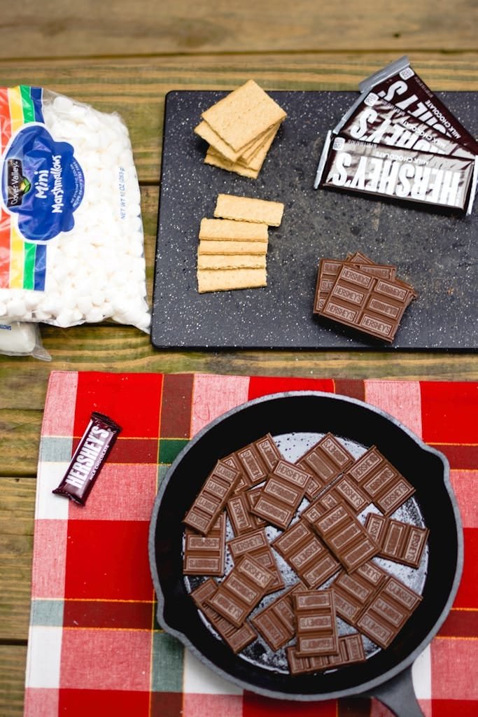 Preparing s'mores outdoors with chocolate, graham crackers, and marshmallows.