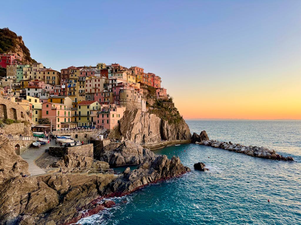 Scenic view of Manarola, Liguria with colorful houses perched on rocky cliffs at sunset.