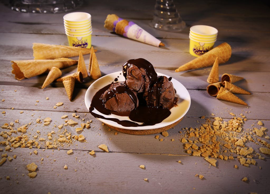 Scoops of chocolate ice cream with syrup and waffle cones on a rustic table.