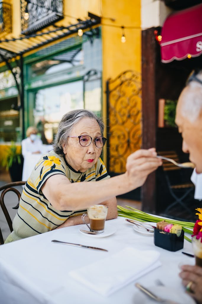 Senior Asian couple sharing a moment at a vibrant outdoor cafe, enjoying coffee together.