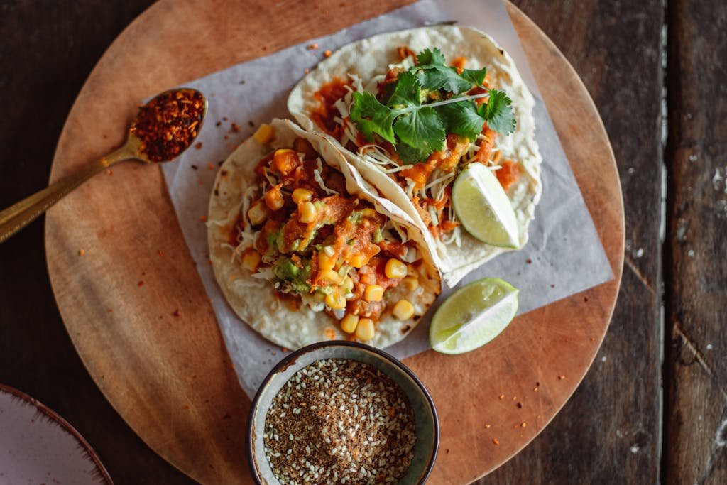 Top view of delicious Mexican tacos with fresh ingredients, lime, and salsa on a wooden plate.